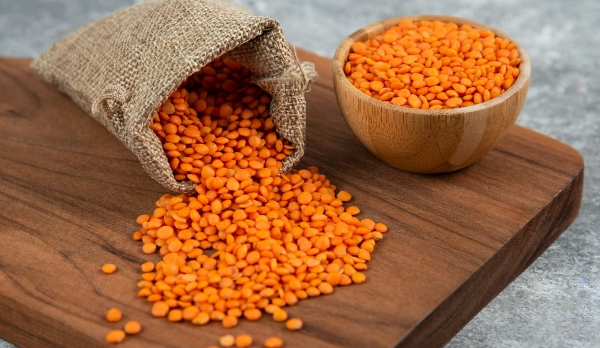 bowl and sackcloth of red raw lentils on a wooden board